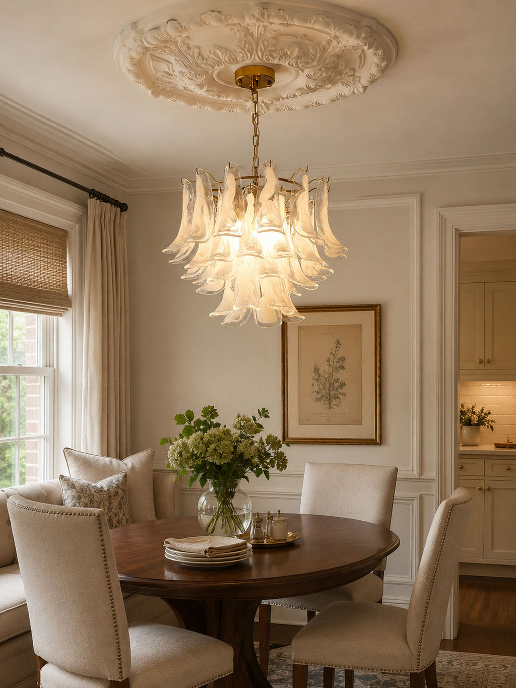 A white frosted glass chandelier from Clérachic hangs below a plaster ceiling rose, above a round table with flowers and plates.