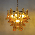 Close view of a Clérachic chandelier with orange-edged amber glass leaves, lit warm against a mustard-toned wall.