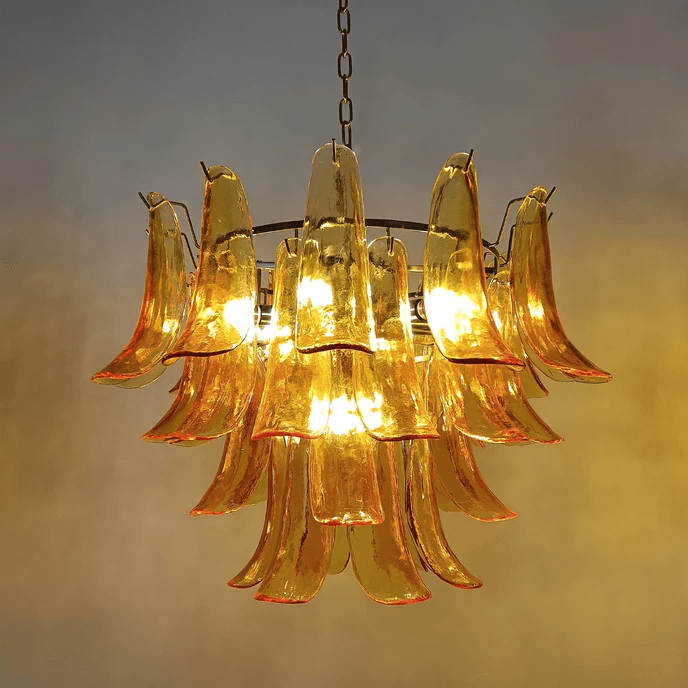 Close view of a Clérachic chandelier with orange-edged amber glass leaves, lit warm against a mustard-toned wall.