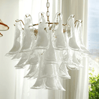 Close view of large clear glass leaves with a milky centre on this Clérachic chandelier, in front of a bright window.