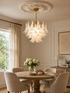 Frosted glass leaves of this Clérachic chandelier glow above a round table with cream chairs and a bowl of white flowers.