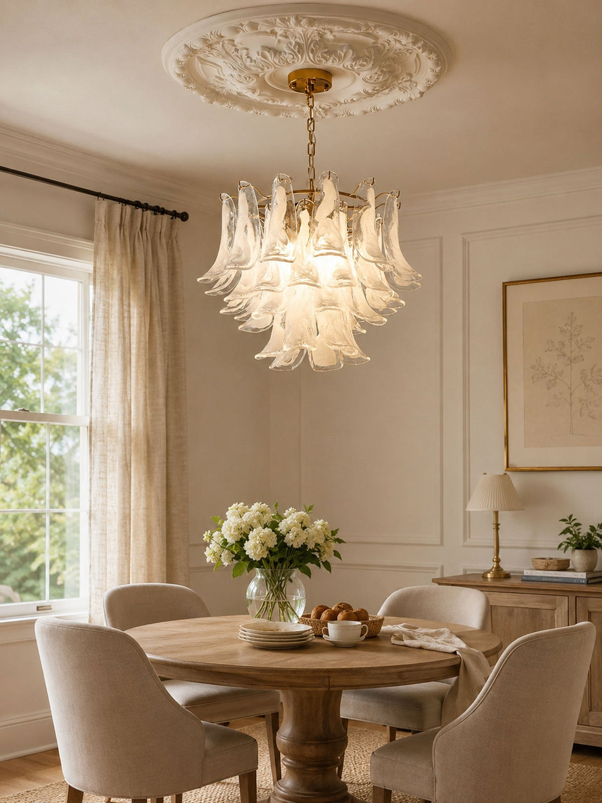 Frosted glass leaves of this Clérachic chandelier glow above a round table with cream chairs and a bowl of white flowers.