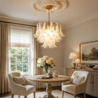 This Clérachic white glass leaf chandelier hangs near a tall window, over a small round table with two armchairs and a teapot.