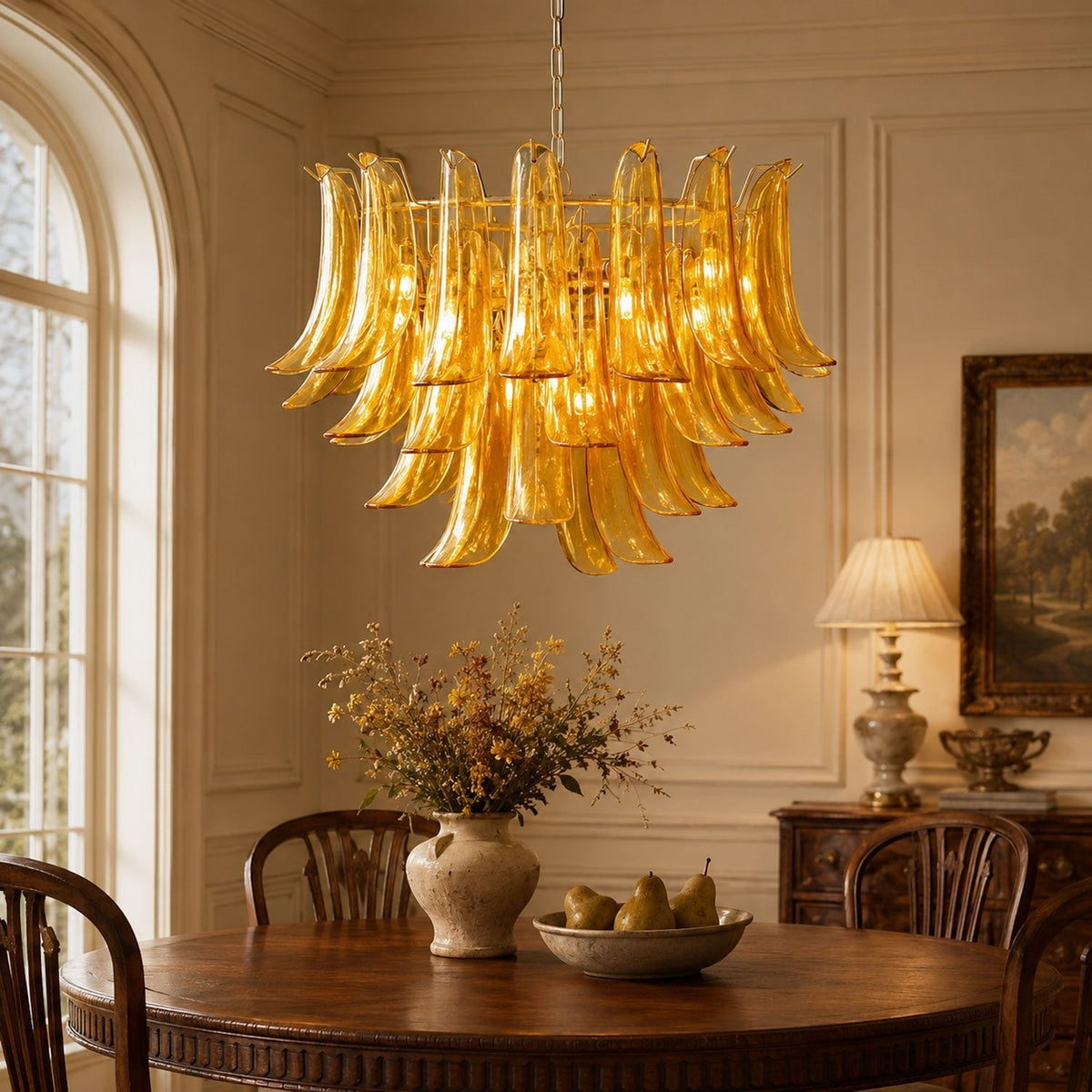Close view of the layered amber glass leaves of this Clérachic chandelier, hanging over a round table with pears and dried flowers.