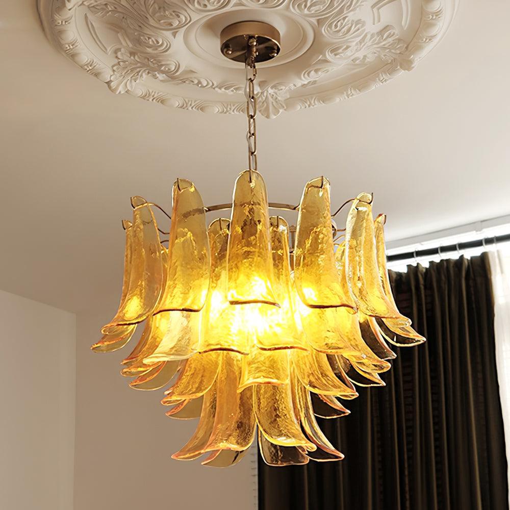 Glowing amber glass leaves in three tiers on this Clérachic chandelier, hung from a decorative plaster ceiling rose beside dark curtains.