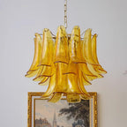 Tiered amber glass leaves with fine gold edges on this Clérachic chandelier, shown near a gilt-framed painting on a pale wall.
