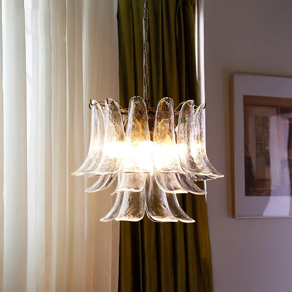 Clear glass leaf chandelier from Clérachic lit against sheer curtains and olive-green drapes, with a framed picture beside it.