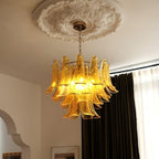 This Clérachic amber glass chandelier hangs from a plaster ceiling rose, with dark curtains and an arched doorway behind.