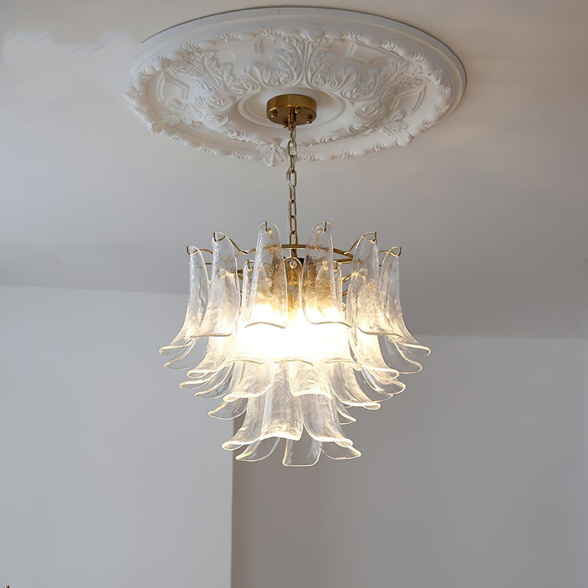 A clear glass leaf chandelier from Clérachic seen from below, unlit, with its brass canopy set against a plaster ceiling rose.