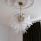 Close view of the clear, rippled glass leaves of this Clérachic chandelier, hanging near olive-green velvet curtains.