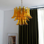 Amber glass leaf chandelier from Clérachic hanging in front of olive-green curtains, with framed pictures on a white wall below.