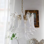 Close view of the large clear glass leaves of this Clérachic chandelier, beside a gilt picture frame and a small plaster bust.