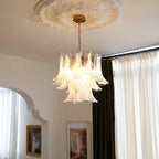 Soft glow from a white cloud glass leaf Clérachic chandelier, hanging under a plaster ceiling rose by an arched doorway.