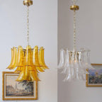 Two Clérachic chandeliers side by side, one in amber glass and one in clear glass, each hanging from a brass canopy on a chain.