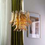 This Clérachic amber glass chandelier hangs in front of green and white curtains, with a framed print on the wall at its right.