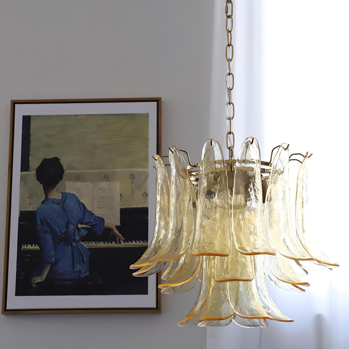 Pale amber and clear glass leaves on a Clérachic chandelier, lit beside a framed painting of a woman at a piano.