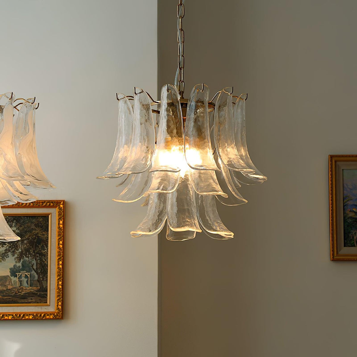 Clear glass leaf chandelier from Clérachic glowing warm in a corner, with gilt-framed paintings on the walls either side.