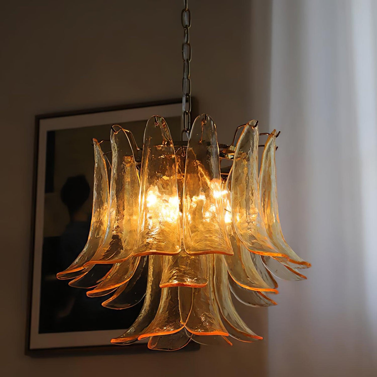 Close view of a Clérachic chandelier with amber-edged glass leaves lit from within, against a dark framed picture.