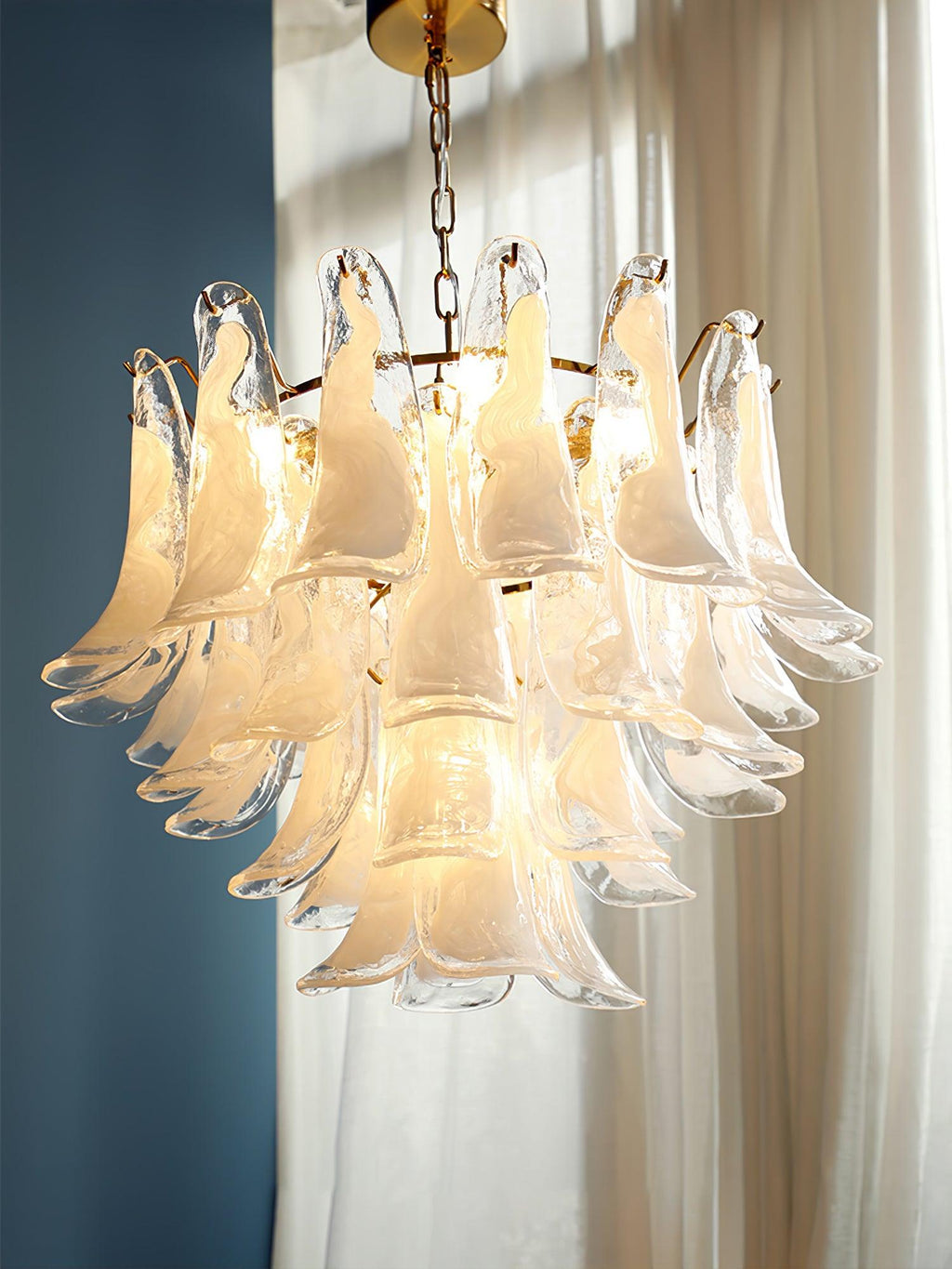Looking at the white cloud glass leaves of this Clérachic chandelier, lit warm in front of a blue wall and sheer curtains.