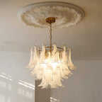 White cloud glass chandelier from Clérachic glowing under a plaster ceiling rose, with soft window light on the wall below.