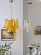 Two Clérachic chandeliers hang side by side, one in amber glass and one in clear glass, by gold-framed paintings and flowers.
