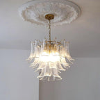 Clear glass leaf chandelier from Clérachic lit warm white, hanging from a brass canopy beneath a round plaster ceiling rose.