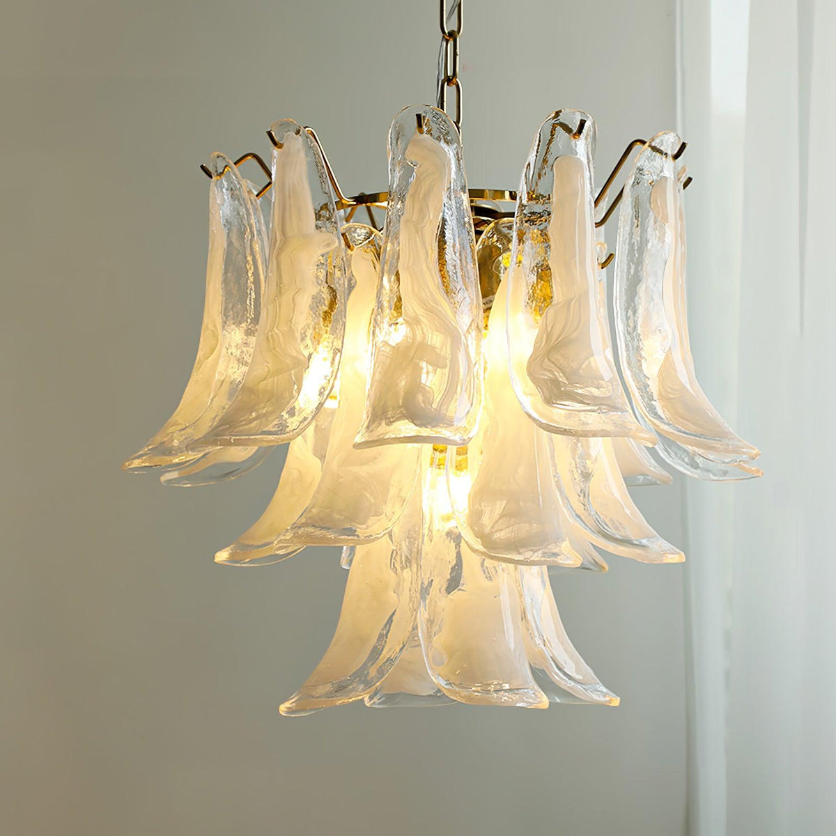 Close view of the thick, milky glass leaves on this Clérachic chandelier, lit warm in front of a sheer curtain.
