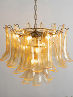 Close view of amber glass leaves with gold edges lit from inside this Clérachic chandelier, hanging on a long chain.