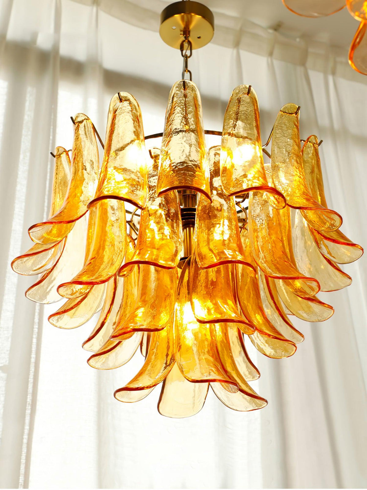 Looking up into this Clérachic chandelier, the orange-edged amber glass leaves glow against sunlit curtains.