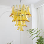 Tall tiered chandelier of yellow glass leaves hanging in a white room with a fern in the lower corner, from Clérachic.
