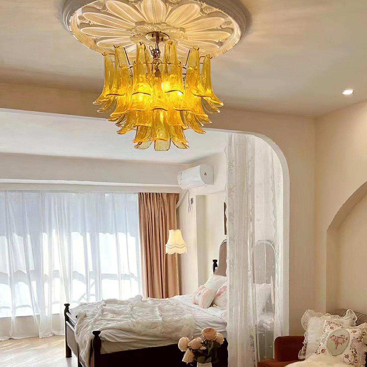 Amber glass leaf chandelier from Clérachic under a flower-shaped ceiling rose, with an arched opening to a bedroom behind.