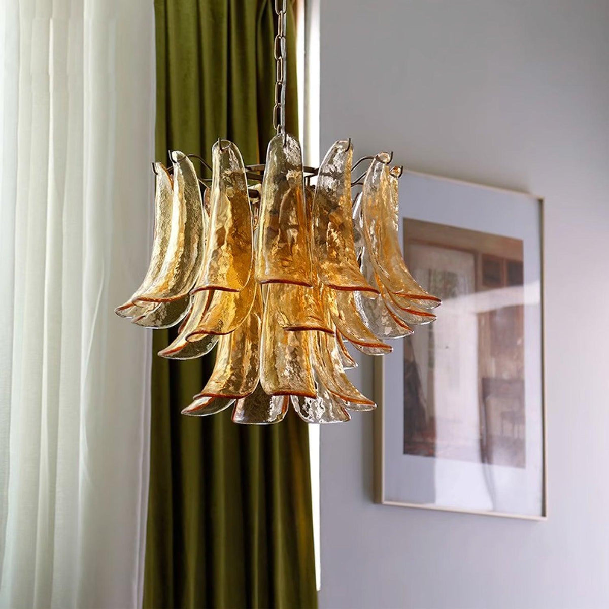This Clérachic chandelier of smoky amber glass leaves hangs in front of olive-green drapes and a large framed print.