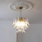 Clérachic clear glass chandelier lit from below, hanging from a brass canopy under a round ornate plaster ceiling rose.