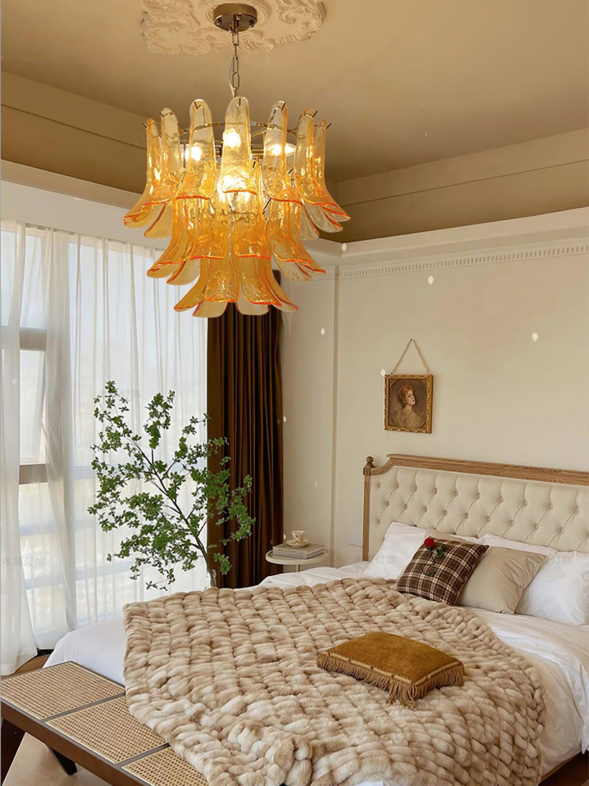 Amber glass leaf chandelier from Clérachic over a bed with a woven throw, a tufted headboard and a leafy branch in a vase.