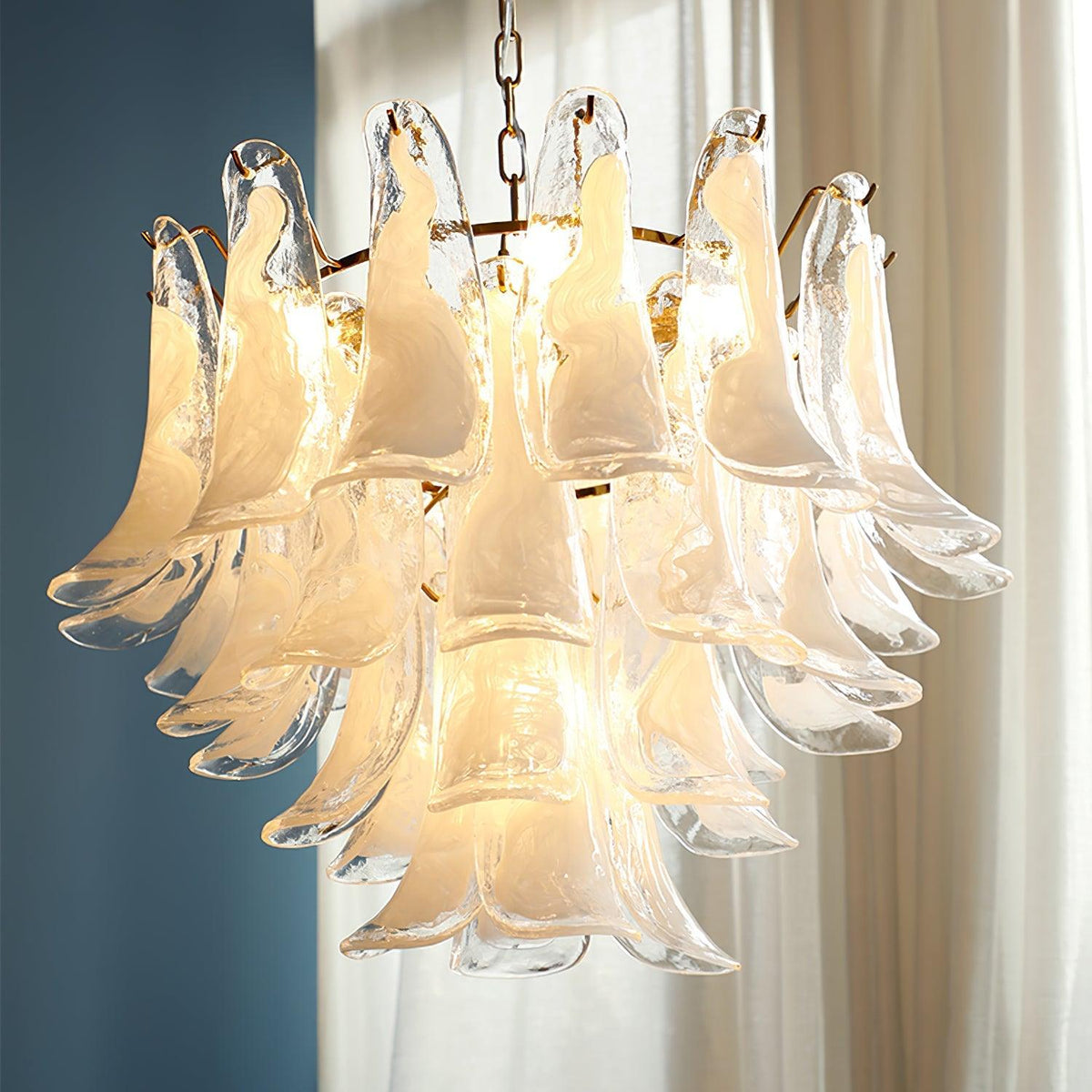 Close view of milky white cloud glass leaves lit warm on this Clérachic chandelier, set against a blue wall and sheer curtains.