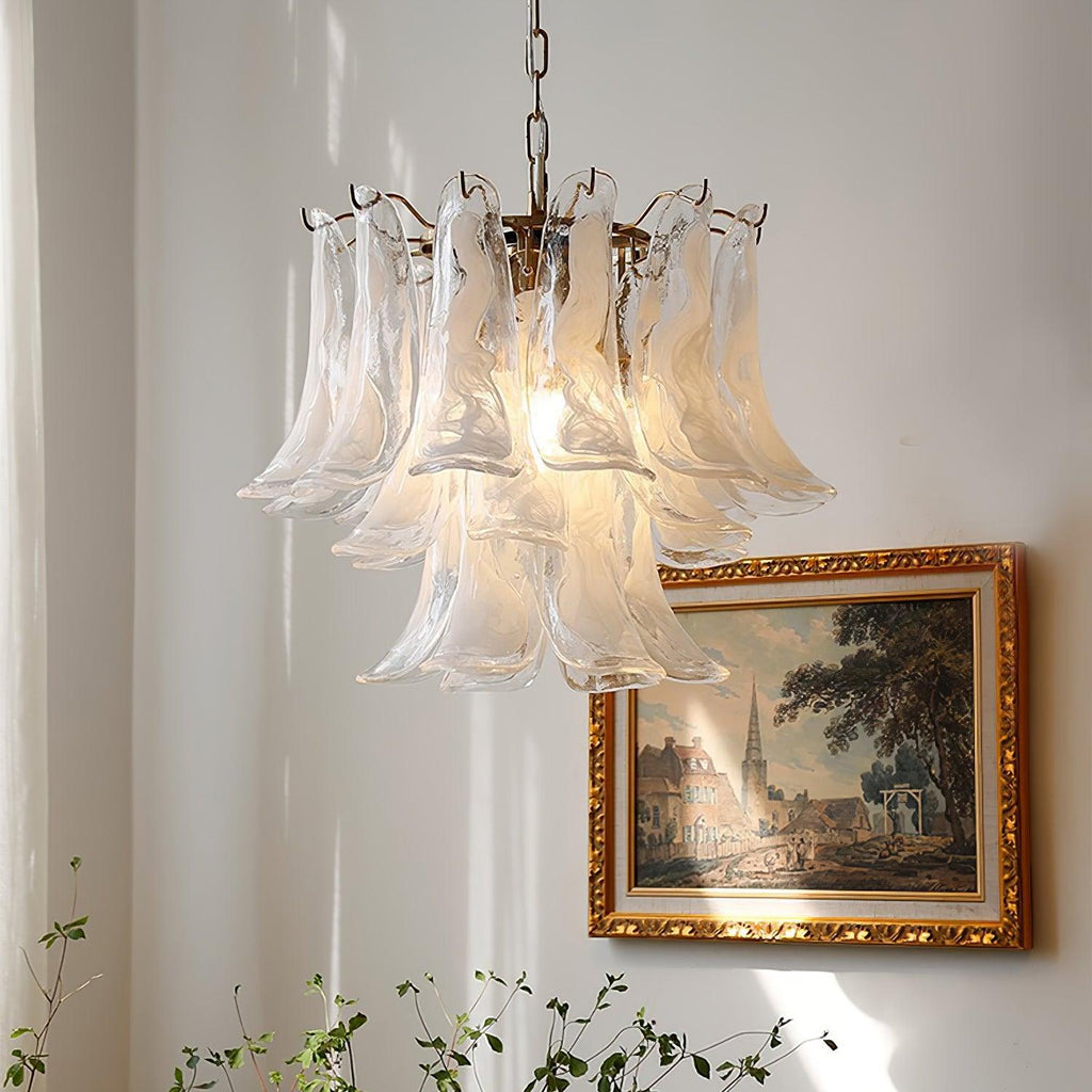 Frosted white glass leaves on a Clérachic chandelier, hanging near a gold-framed village painting with thin green stems below.