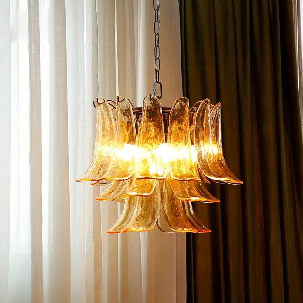 Amber glass leaf chandelier from Clérachic lit warm between sheer white curtains and a dark olive drape.