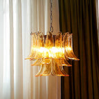 Amber glass leaf chandelier from Clérachic lit warm between sheer white curtains and a dark olive drape.