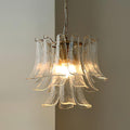 This Clérachic clear glass leaf chandelier glows warm against a taupe wall, its brass ring holding the tiers of glass.
