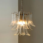 This Clérachic clear glass leaf chandelier glows warm against a taupe wall, its brass ring holding the tiers of glass.
