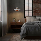 In a dark bedroom with a brick wall, a cream Clérachic pendant glows above a grey bed and a wooden bedside table.