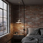 A lit Clérachic pendant warms an exposed brick wall beside a city-view window and a dark grey bed.