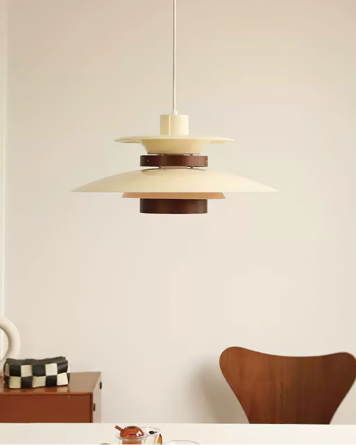 A beige Clérachic pendant hangs in a bright room, with a wooden chair and a checked cushion below.