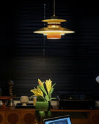 In a dark room with slatted blinds, a lit Clérachic pendant glows amber above a sideboard with yellow lilies.