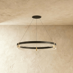 A Clérachic ring chandelier in black with brass connectors and a ribbed acrylic diffuser hangs from a plaster ceiling.