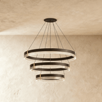 Three cascading rings on the Clérachic chandelier descend in graduated sizes, each edged in brass and warm light.