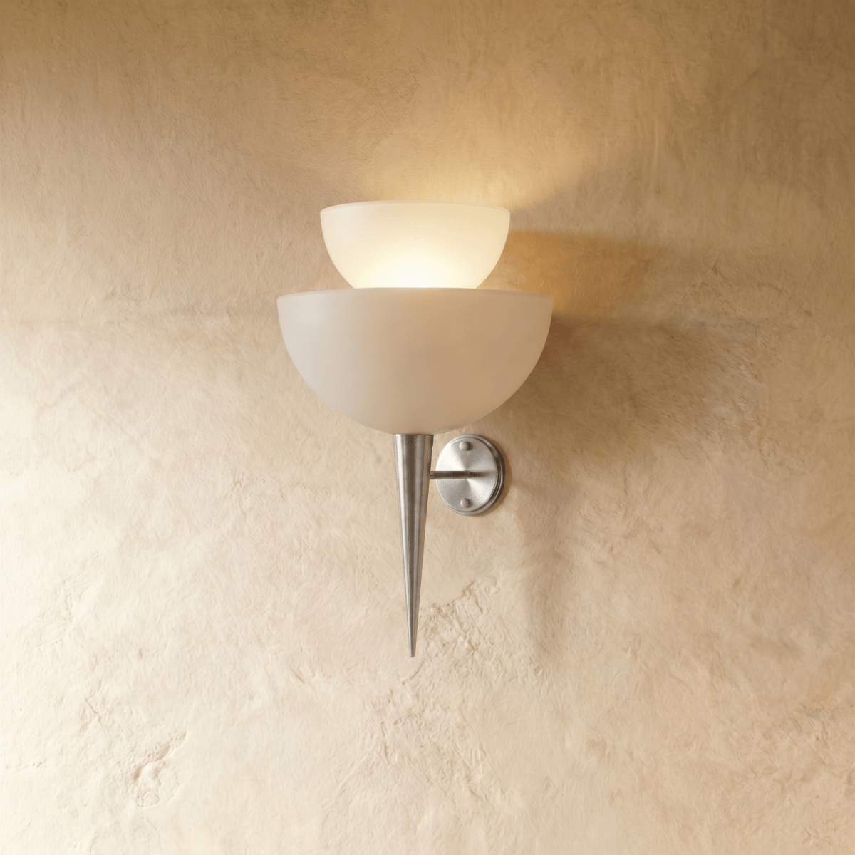 Clérachic wall lamp in chrome, two tiered frosted glass shades glowing above a slender pointed base.