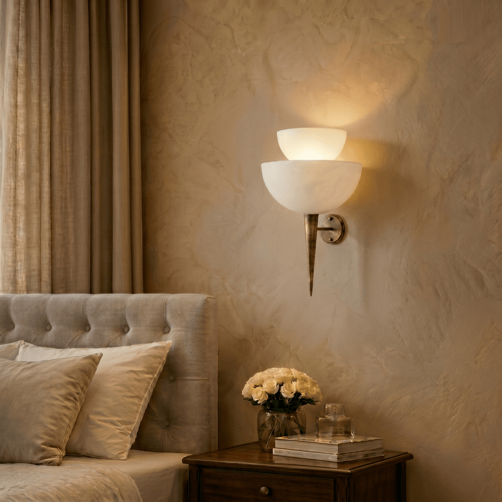 Clérachic wall lamp in brass lighting a bedroom nightstand set with a vase of white roses and books.