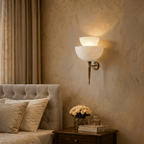 Clérachic wall lamp in brass lighting a bedroom nightstand set with a vase of white roses and books.