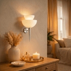 Clérachic wall lamp in chrome glowing beside a side table with a lit candle and sheer curtains.